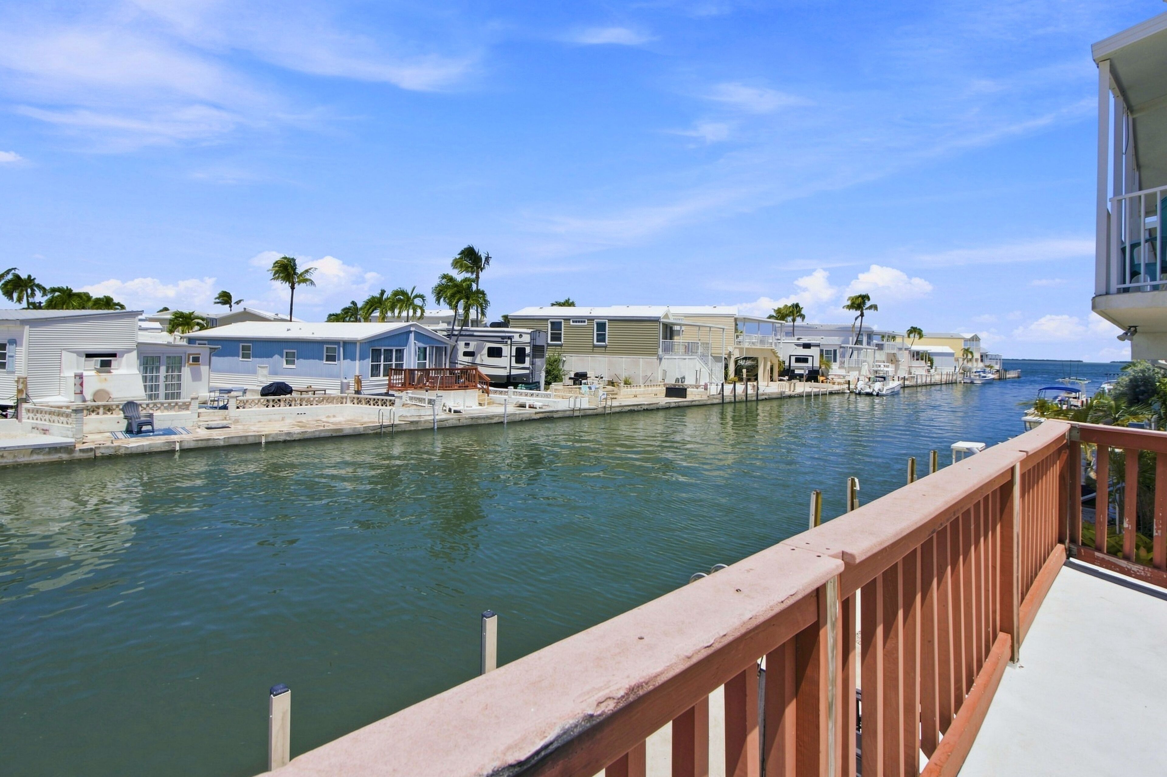 A marina with RVs docked along a calm waterway, surrounded by palm trees and a clear sky.
