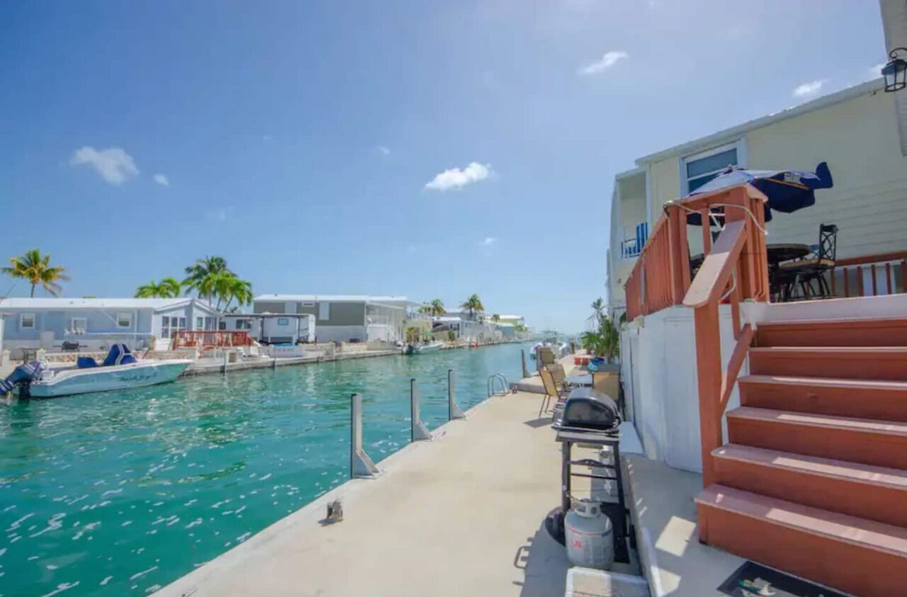 Un puerto deportivo con barcos amarrados, una vía fluvial y un edificio con porche y terraza.