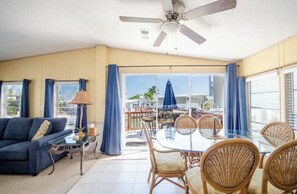Relax in this inviting living area with a high ceiling fan, sofa, and dining table, offering a view of the balcony with outdoor furniture.