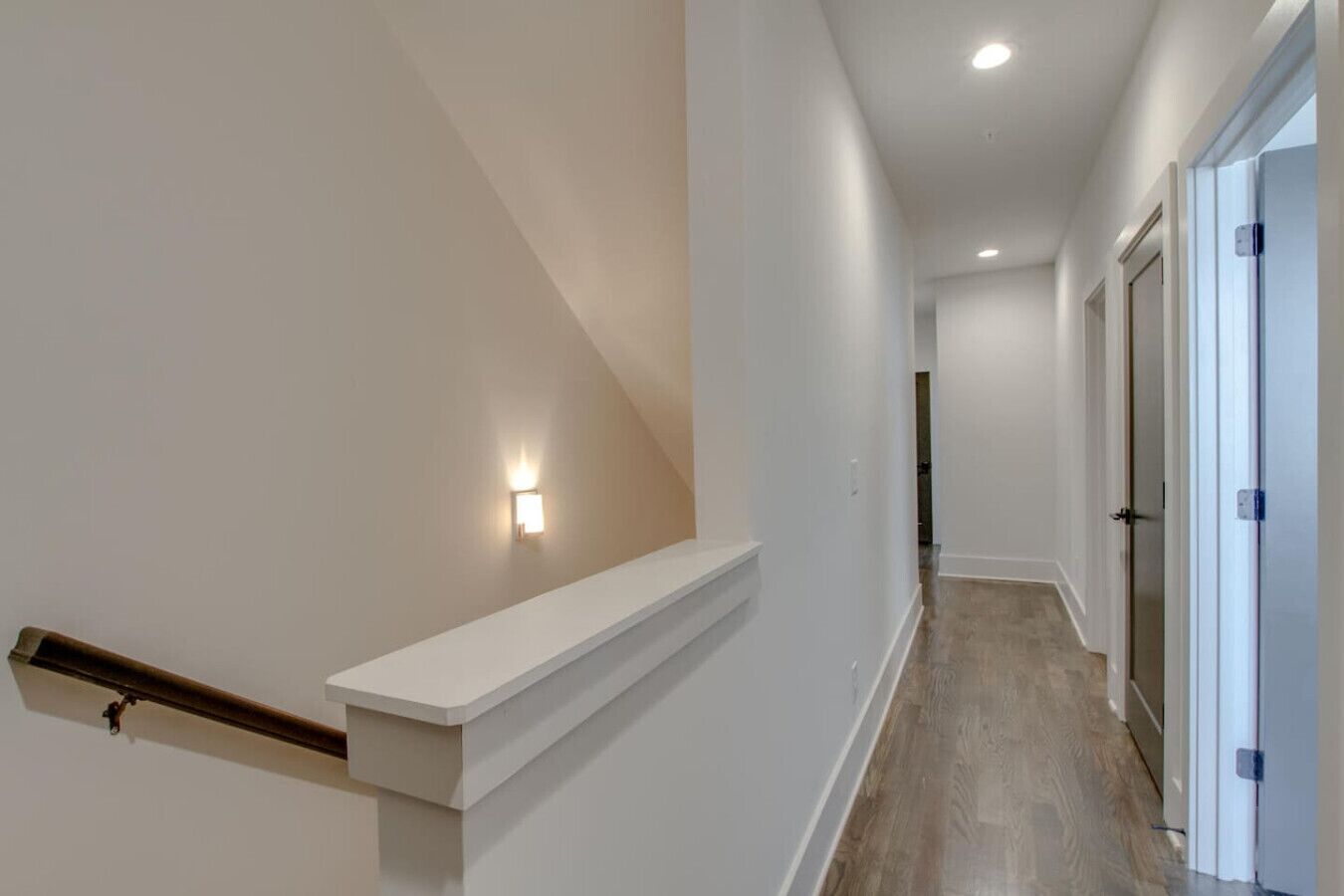 Un couloir moderne avec un escalier en bois, des murs blancs et un luminaire.