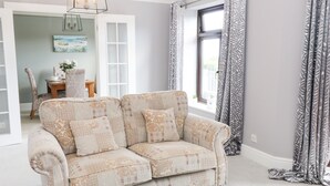Un salón con un sofá estampado, una mesa de comedor con sillas y una ventana con cortinas.