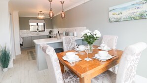 Cocina moderna con comedor, mostrando una mesa de madera dispuesta para cuatro personas, con platos y vasos blancos.