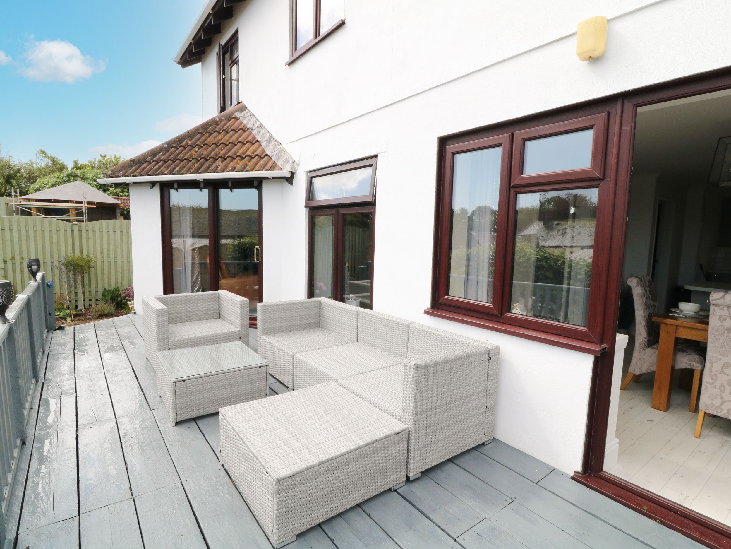 Un patio con mobiliario de mimbre, una terraza de madera y una casa blanca con marco de ventana marrón.