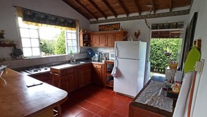 A kitchen with wooden cabinets, a white refrigerator, a sink, and a window with a curtain. - Ideal chalet: tourism in the coffee region with swimming pool. (Ulloa)
