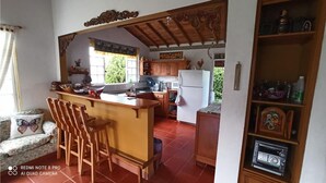 A kitchen with wooden cabinets, a white refrigerator, a sink, and a bar area with stools. - Ideal chalet: tourism in the coffee region with swimming pool. (Ulloa)