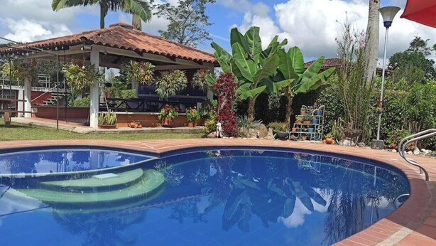 A swimming pool with a tiled deck, surrounded by lush greenery and a gazebo. - Ideal chalet: tourism in the coffee region with swimming pool. (Ulloa)