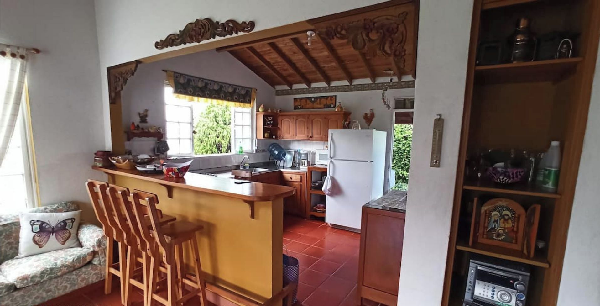 Une cuisine avec des meubles de rangement en bois, un réfrigérateur blanc, un évier et un coin bar avec des tabourets.