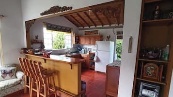 Une cuisine avec des meubles de rangement en bois, un réfrigérateur blanc, un évier et un coin bar avec des tabourets.