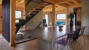 A modern interior with a central dining area, a staircase, and a view of a blue sofa in the background. - Chalet Les P'tits Biquets  (GERARDMER)