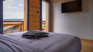 A bedroom with a bed, a TV mounted on the wall, and a large window offering a view of the outdoors. - Chalet Les P'tits Biquets  (GERARDMER)
