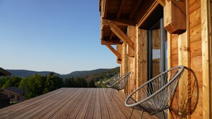 A wooden deck with two metal chairs, overlooking a forested valley. - Chalet Les P'tits Biquets  (GERARDMER)