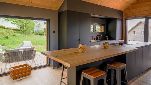 A modern kitchen with a wooden island, bar stools, and a view of the outdoors. - Chalet Les P'tits Biquets  (GERARDMER)