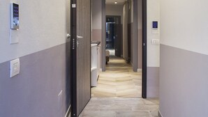 A modern hotel corridor with a light-colored floor, a wooden ceiling, and a door leading to a bathroom.