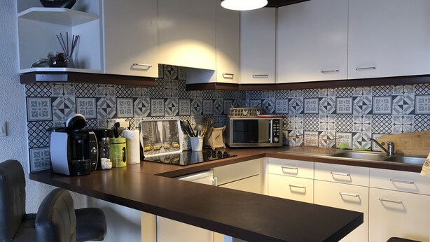A modern kitchen with white cabinets, a black countertop, a microwave, and a coffee maker. - Charmant Zola (Troyes)