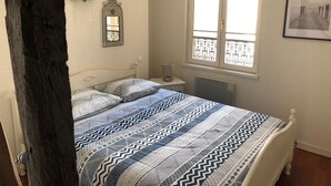 A bedroom with a bed, a nightstand, a radiator, a window with a view, and a wall-mounted mirror. - Charmant Zola (Troyes)
