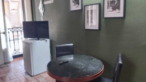 Una habitación pequeña con una mesa redonda, dos sillas, un televisor sobre un mueble blanco y tres cuadros en la pared.