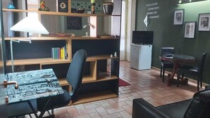 Una habitación acogedora con escritorio, silla, estantería y una pequeña televisión.