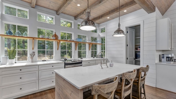Una cocina amplia con armarios blancos, una isla grande, sillas de madera y un colgante.