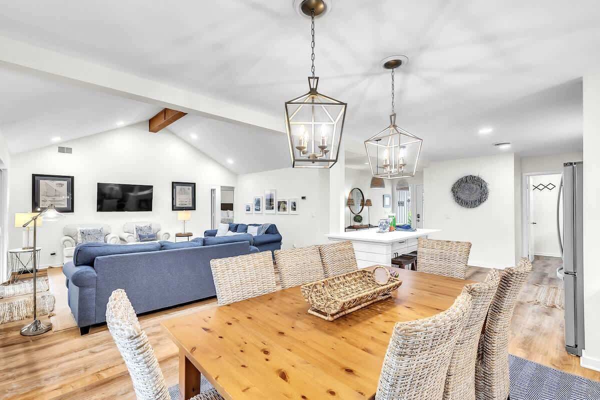 A spacious living area with a wooden dining table, wicker chairs, a blue sofa, and pendant lighting.