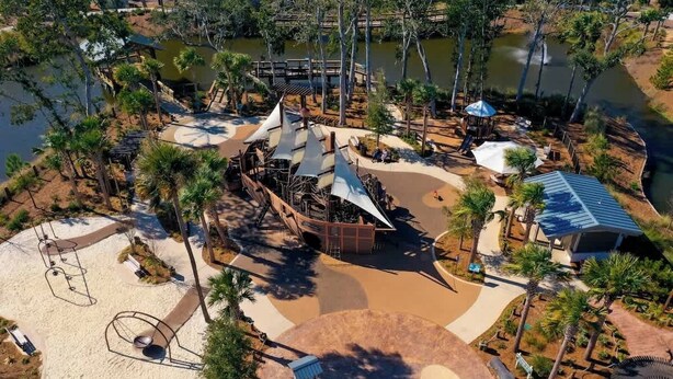 Luchtbeeld van een park met een zandgebied, een waterpartij en een beschaduwd paviljoen.