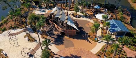 An aerial view of a park with a sandy area, a water feature, and a shaded pavilion.