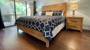 Een slaapkamer met een bed, houten nachtkastjes, een plafondventilator en een uitzicht door een groot raam.