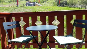 Un balcón con dos sillas plegables y una pequeña mesa, con vistas a un paisaje montañoso con un telesilla y un edificio que dice "Le Montagne".