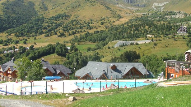 Un complejo turístico de montaña con piscina, edificios de estilo chalet y vistas de las colinas circundantes.