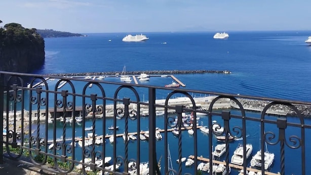 A marina with several boats docked, a clear blue sky, and a rocky coastline. - SMALL COURT MAISON (Piano di Sorrento)