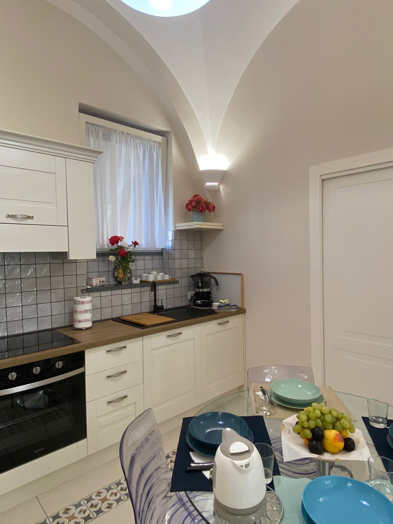 A modern kitchen with white cabinets, a black stove, and a dining area with a glass table set for two.