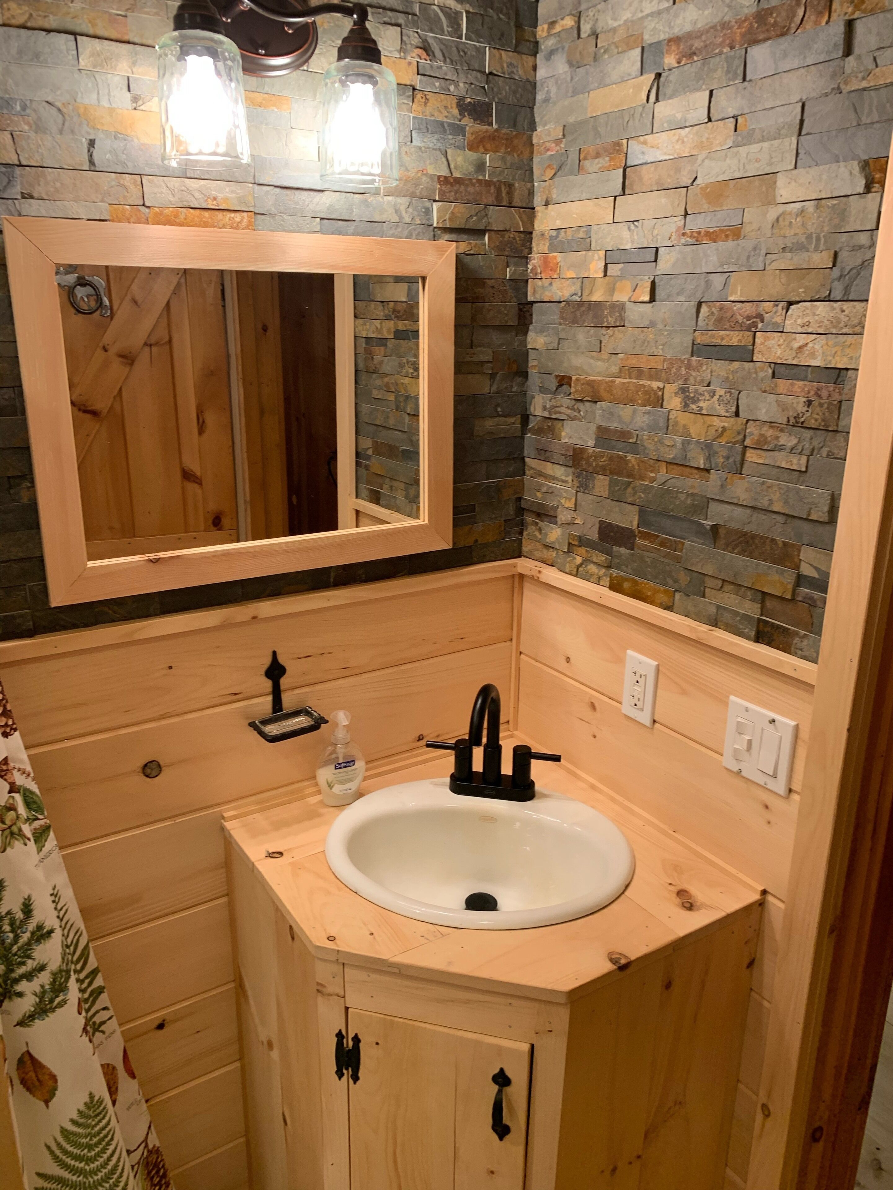 A wooden bathroom with a stone wall, a mirror, a sink, and a faucet.