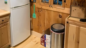A wooden-paneled kitchen with a white refrigerator, a window with a view of greenery, and a trash can with a lid. - Cozy cottage (Lunenburg)