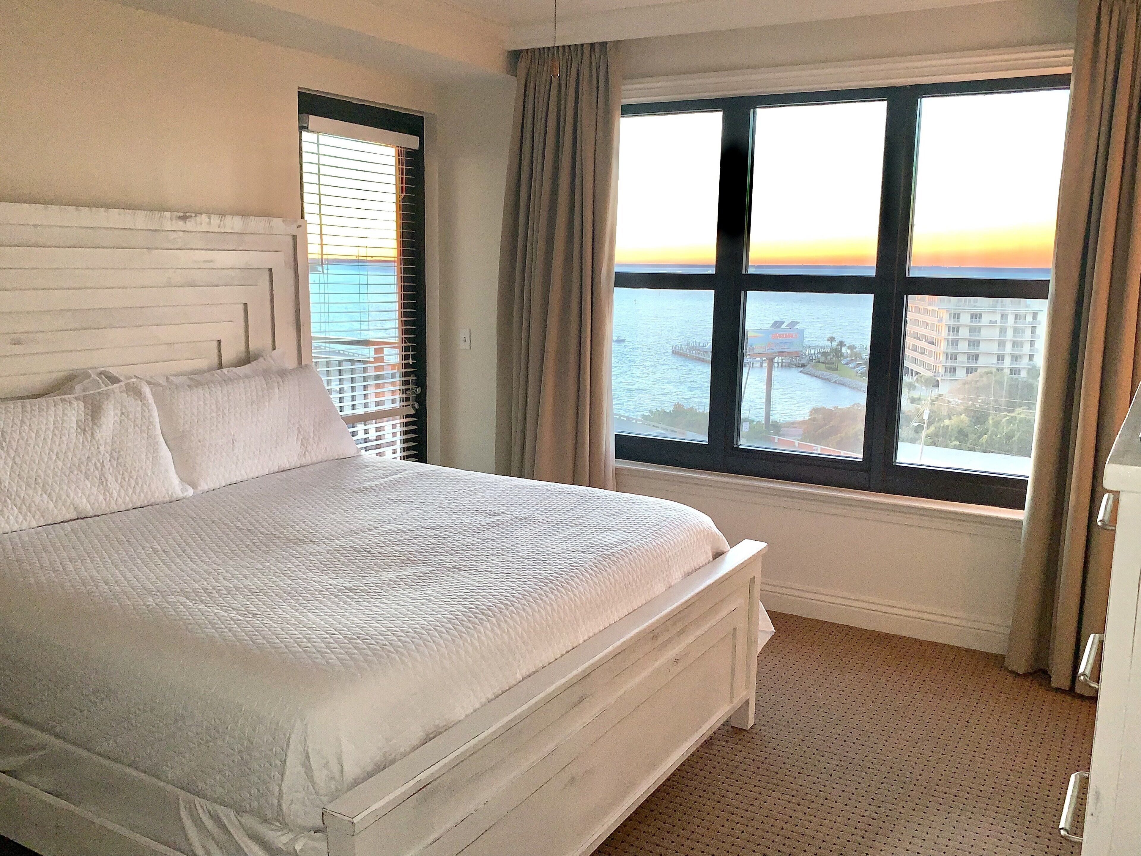 Une chambre d’hôtel avec un grand lit, une vue sur la mer et une fenêtre avec des rideaux.