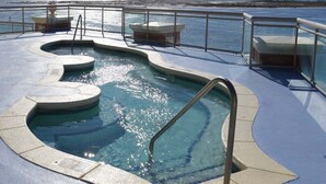 Zona de piscina con barandilla de vidrio, diseño de piscina curvo y vista al océano.