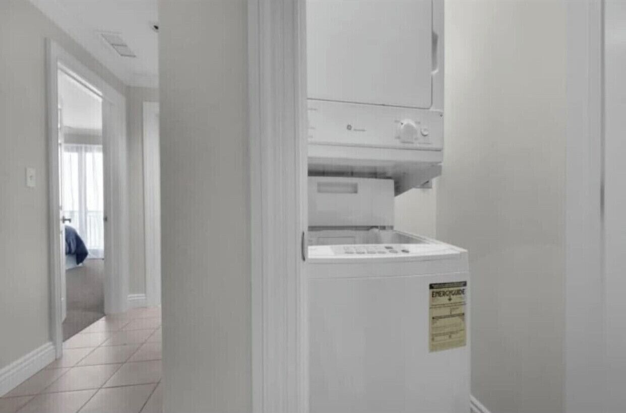 A laundry room with a washing machine and dryer, a sign indicating electrical safety, and a hallway leading to another room.