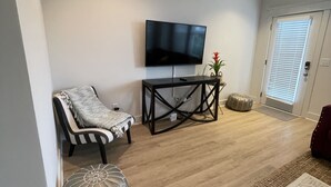 A living room with a flat-screen TV mounted on the wall, a black coffee table, a striped armchair, a grey ottoman, and a patterned rug.