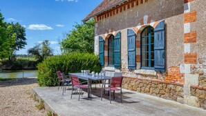 A rustic stone building with a table and chairs set up on a gravel area beside a river. - So Villa Gouadiere (45) - Heated pool - Basketball - 2h Paris - 30p (Poilly-lez-Gien)