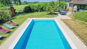 A rectangular swimming pool with a tiled edge, surrounded by a concrete deck. There are lounge chairs along the pool's edge, and a small building with a sloped roof is visible in the background. - So Villa Gouadiere (45) - Heated pool - Basketball - 2h Paris - 30p (Poilly-lez-Gien)