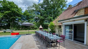 Een zwembadgedeelte met een lange eettafel, klaar voor een maaltijd, een barbecue en een overdekt terras.