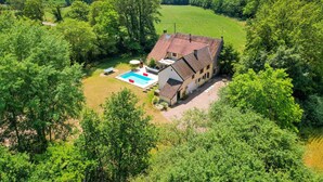 Een tweelaags huis met een zwembad, omringd door weelderige begroeiing en bomen.
