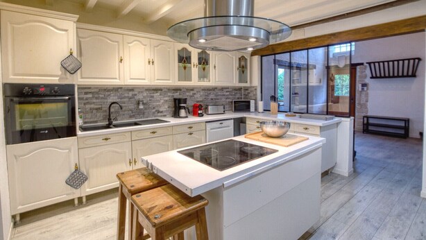 Een moderne keuken met witte kasten, een groot eiland en een roestvrijstalen afzuigkap.