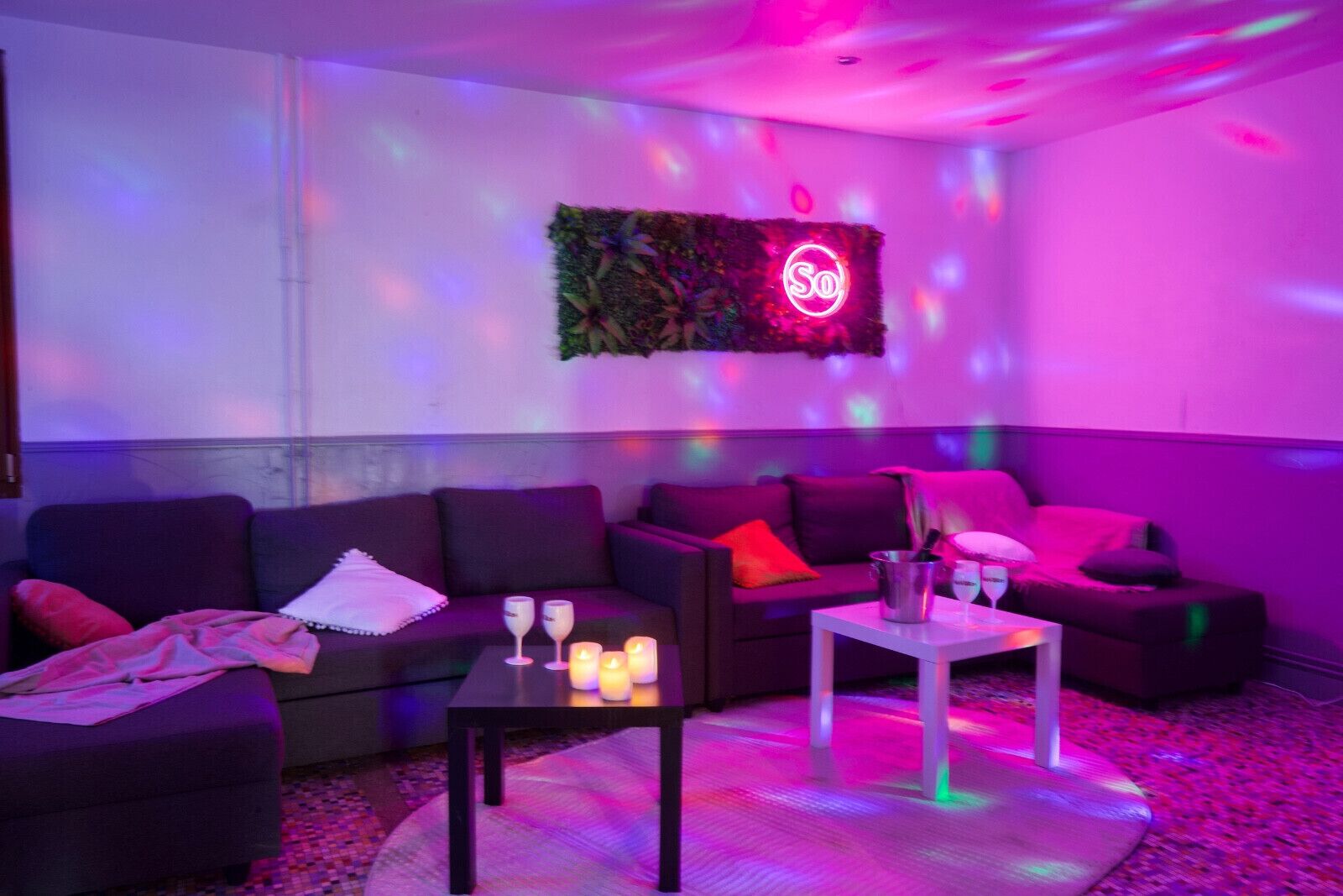 Un espace de détente moderne avec des canapés, une petite table avec des boissons et un éclairage d’ambiance.
