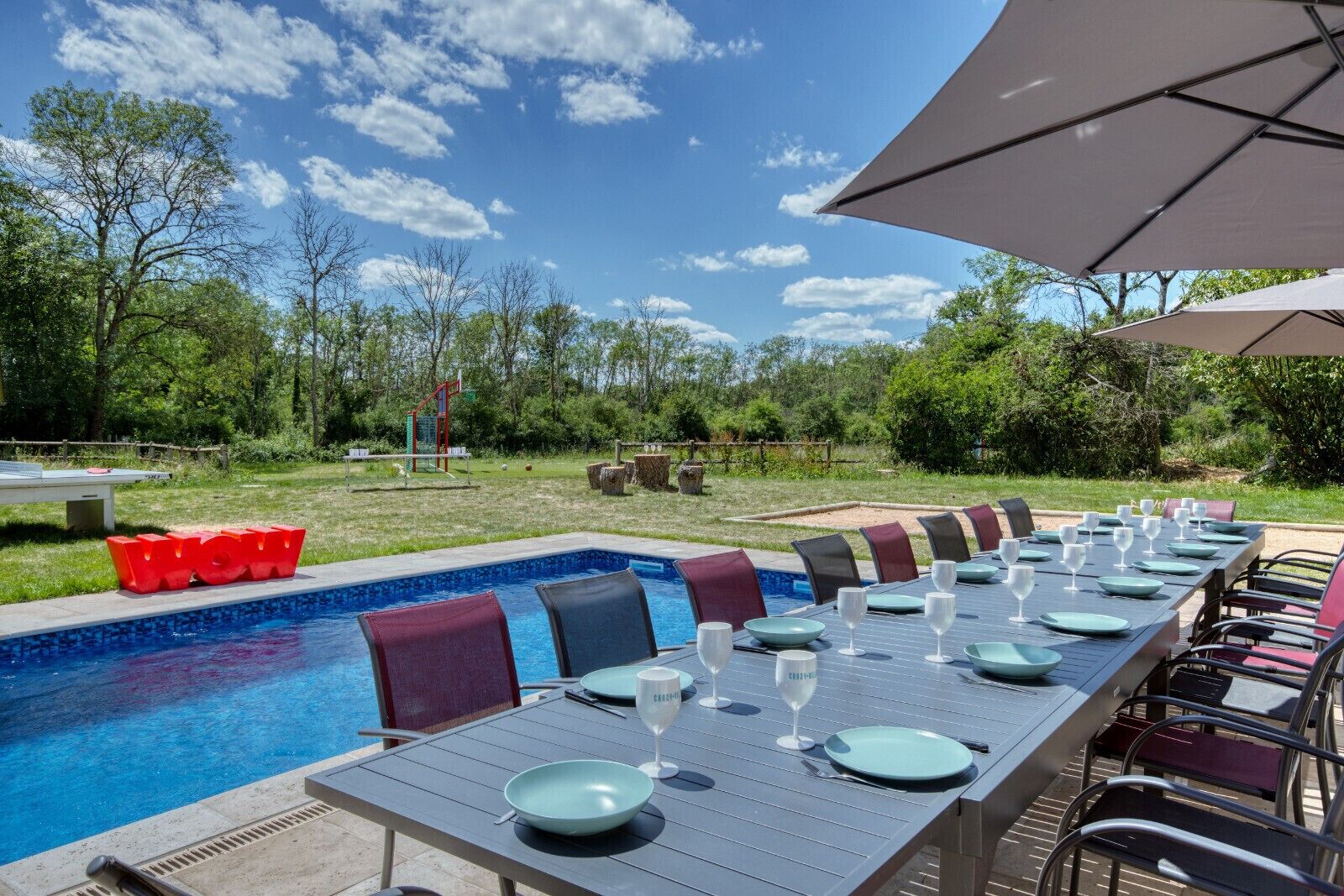 An outdoor dining area with a pool, dining tables, chairs, and umbrellas.