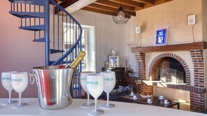 A cozy interior with a brick fireplace, a spiral staircase, and a table with wine glasses and a champagne bottle.