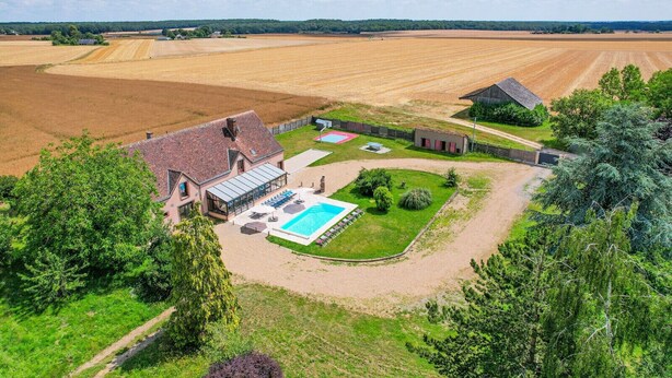 A large house with a swimming pool, surrounded by fields and trees.