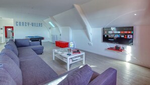 A modern living room with a pool table, a large flat-screen TV, and a sofa.
