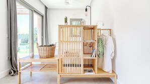 Une pièce lumineuse avec un banc en bois, une armoire en bois dotée d’étagères, un porte-vêtements et une fenêtre avec des rideaux.
