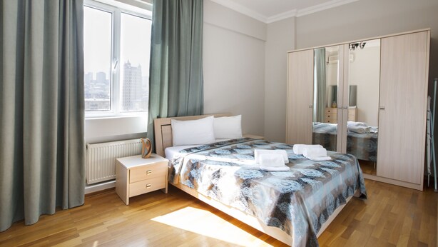 A bedroom with a large bed, a nightstand, a dresser, a mirror, and a window with curtains. - Fountain Square (Baku)