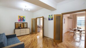 A spacious living room with a wooden floor, a blue sofa, a dining area with a table and chairs, and two paintings on the walls. - Fountain Square (Baku)