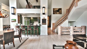 Un amplio espacio habitable con una escalera de madera, una mesa de comedor con sillas y una cocina al fondo.